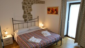 A bedroom with a bed, bedside lamps, a stone accent wall, a painting, and a window with curtains.