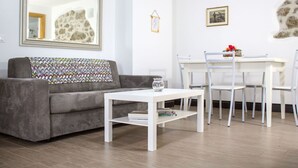 A living room with a grey sofa, a white coffee table, a dining table with white chairs, a framed picture on the wall, and a small decorative item on the table.