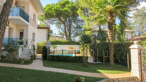 A residential building with a pool, surrounded by greenery and palm trees.