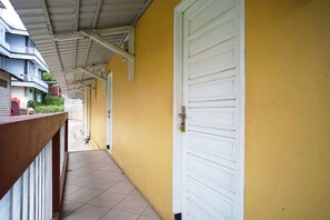 A corridor with yellow walls, a white door, and a balcony with a metal railing.