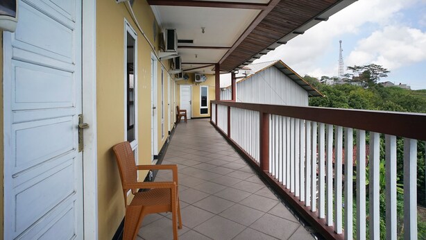 A covered balcony with a tiled floor, white railings, and a row of closed doors on one side.