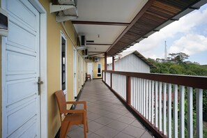 A covered balcony with a tiled floor, white railings, and a row of closed doors on one side.
