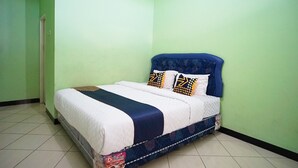 A neatly made bed with a blue headboard and patterned pillows, set in a room with green walls and tiled flooring.