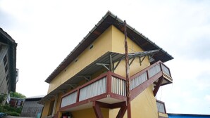 A yellow building with a balcony and a staircase leading to the entrance.