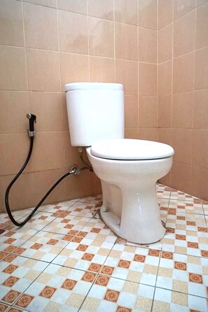 A toilet with a bidet attachment in a bathroom with checkered floor tiles.
