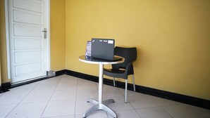 A small, round table with a laptop and a chair in a corner of a room with yellow walls and a white door.