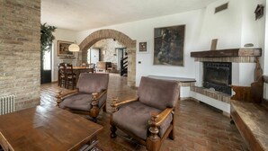 A spacious living room with brick walls, a fireplace, and a dining area with wooden furniture. - Beautiful apartment in villa for 4 guests with A/C, pool, WIFI, TV and terrace (Povoletto)