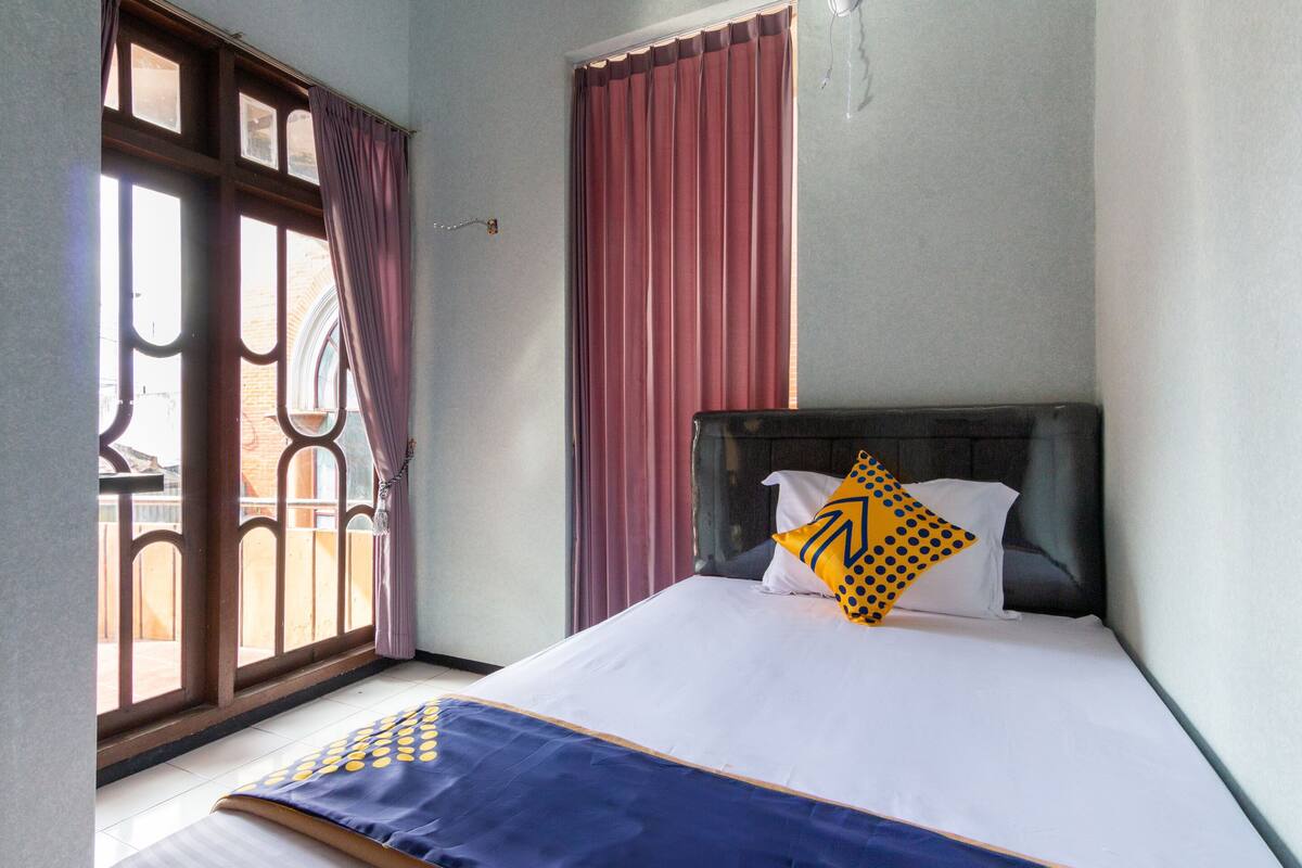 Una habitación de hotel con cama, ventana con cortinas y vista al exterior.
