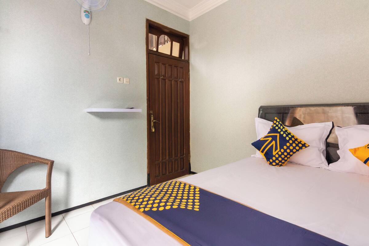 Una habitación con una cama, una silla, una puerta y un pequeño estante.
