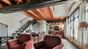 A spacious living area with a wooden staircase, red armchairs, and a view of the kitchen through large windows. - Cosy apartment in villa for 4 guests with A/C, pool, WIFI, TV and terrace (Povoletto)