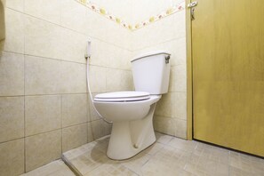 A bathroom with a toilet, a shower, and a yellow door. - OYO 2728 Sinulingga Residence (Bandung)