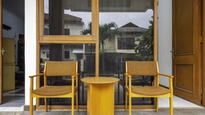 Duas cadeiras de madeira e uma mesa redonda pequena em um quarto com janelas amplas.