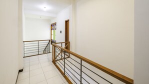 Uma escada com corrimão de madeira e balaústres de metal, que conduz a um quarto com paredes brancas e chão em azulejos.