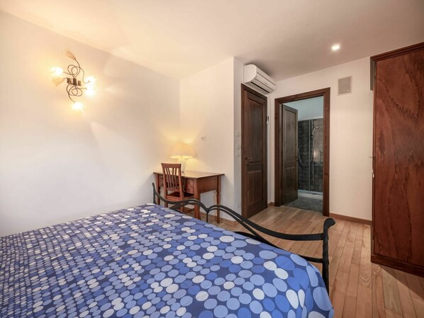 A bedroom with a bed, a desk, and a chair. There is a door leading to a bathroom and a shower.