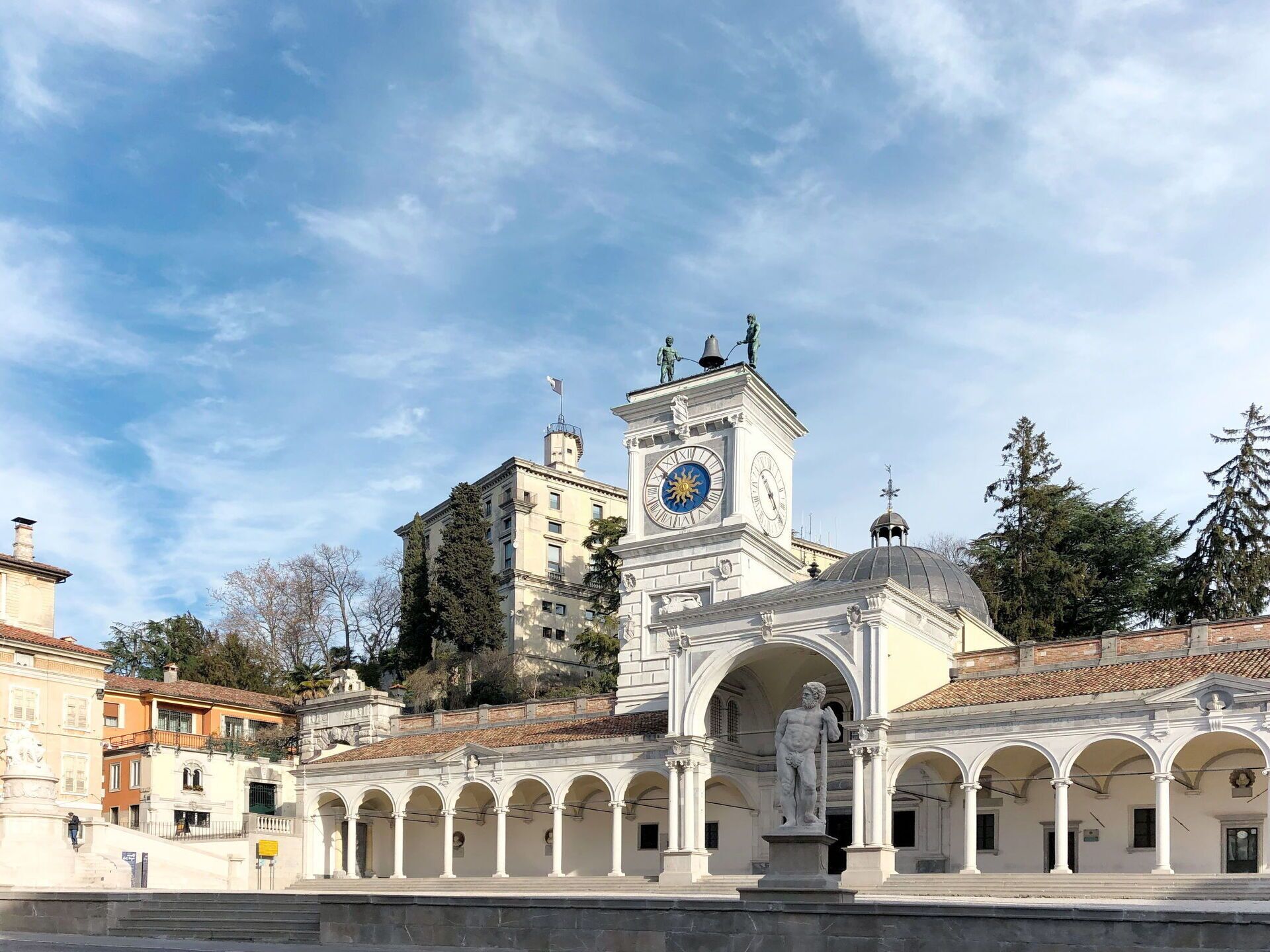 A historic building with a clock tower, statues, and an arched colonnade.