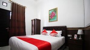 A neatly made bed with a red and white bedspread, a nightstand with a lamp, and a painting of flowers on the wall. - OYO 2630 Wisma Fahza Syariah (Bandar Lampung)