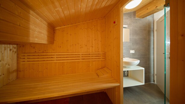 Eine Holzsauna mit Bänken, einem Waschbecken und einer Glastür zum Badezimmer.