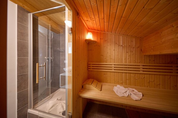 Una sauna de madera con un área de ducha acristalada y un banco.