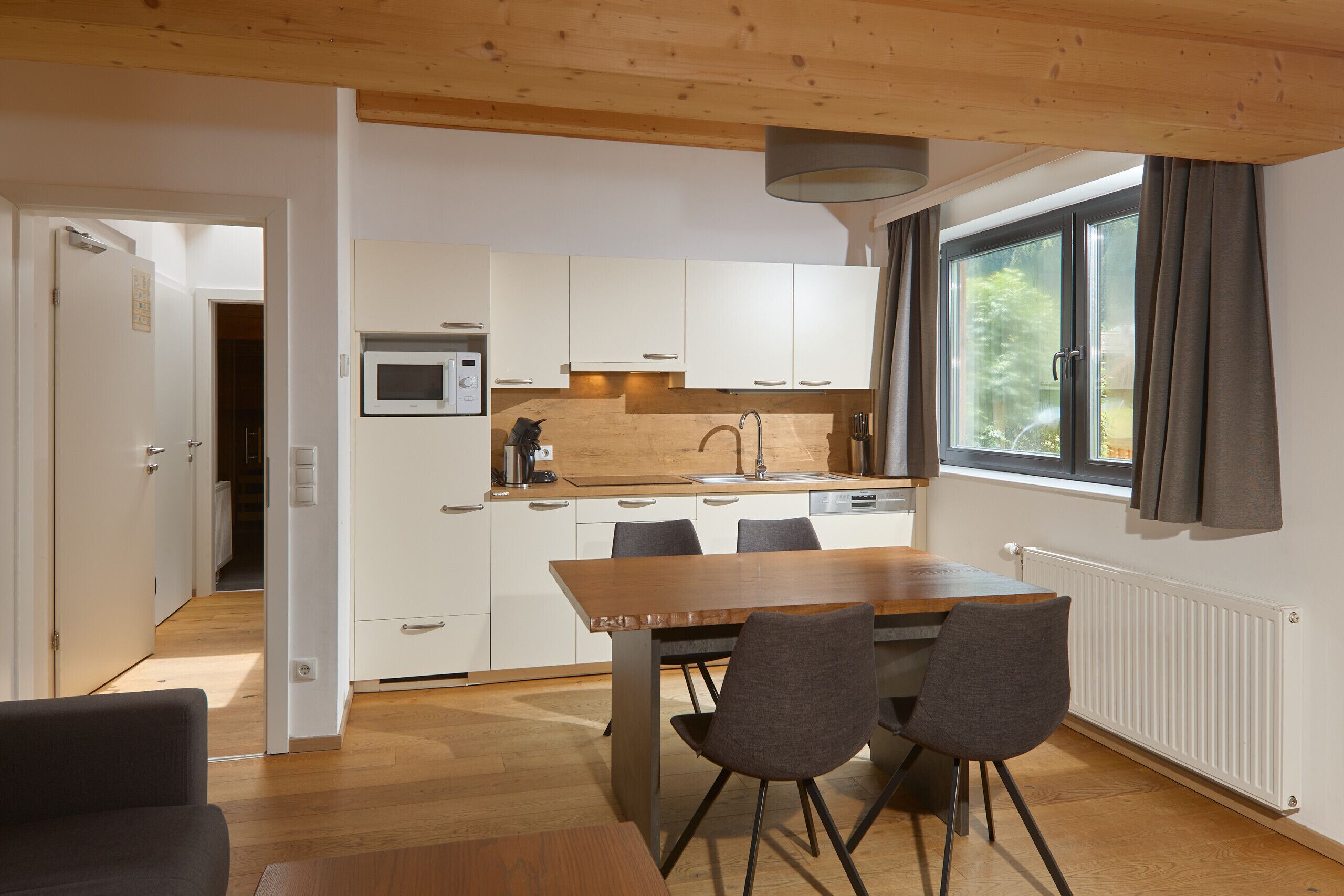 Een moderne keuken met witte kasten, een houten eettafel en twee stoelen.