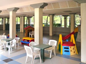 A covered outdoor area with tables and chairs, a children's play structure, and a small wooden house.