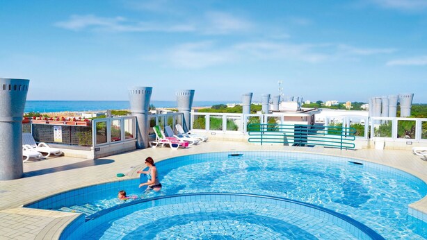 Une piscine sur le toit avec vue sur la mer, des chaises longues et une personne nageant avec un enfant.