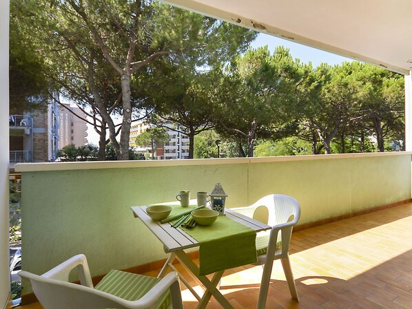 A balcony with a table and chairs, overlooking a tree-lined area with buildings in the background.