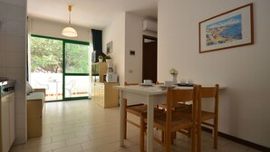 A modern kitchen with a dining area, a view through a glass door, and a painting on the wall. - Beautiful apartment for 6 people with pool, A/C, TV, balcony and pets allowed (Bibione)