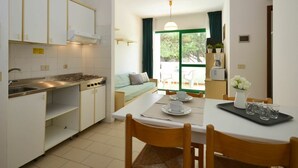 A compact kitchen with white cabinets, a gas stove, and a dining area with a table set for two. - Beautiful apartment for 6 people with pool, A/C, TV, balcony and pets allowed (Bibione)