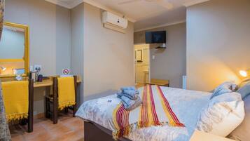 Una habitación de hotel con cama, escritorio, silla, espejo y televisor.