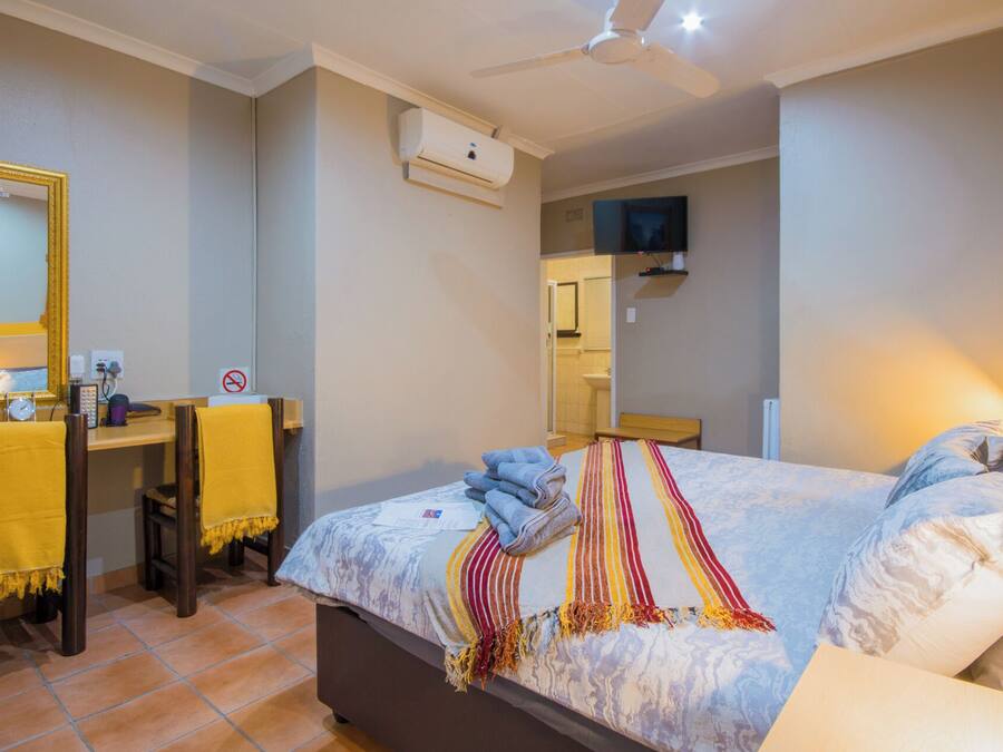 Una habitación de hotel con cama, escritorio, silla, espejo y televisor.