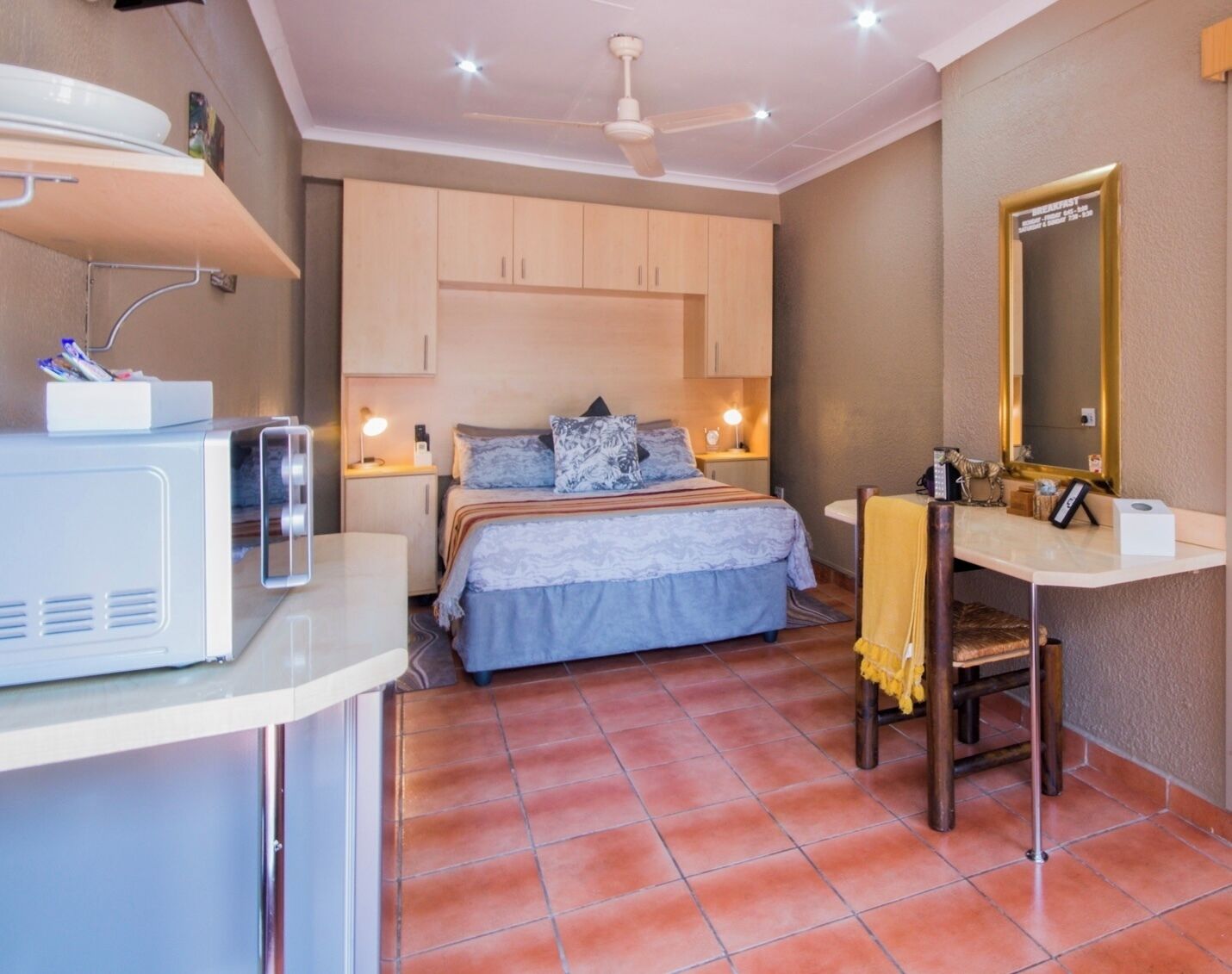 Un dormitorio con cama, mesita de noche, lámpara y espejo.