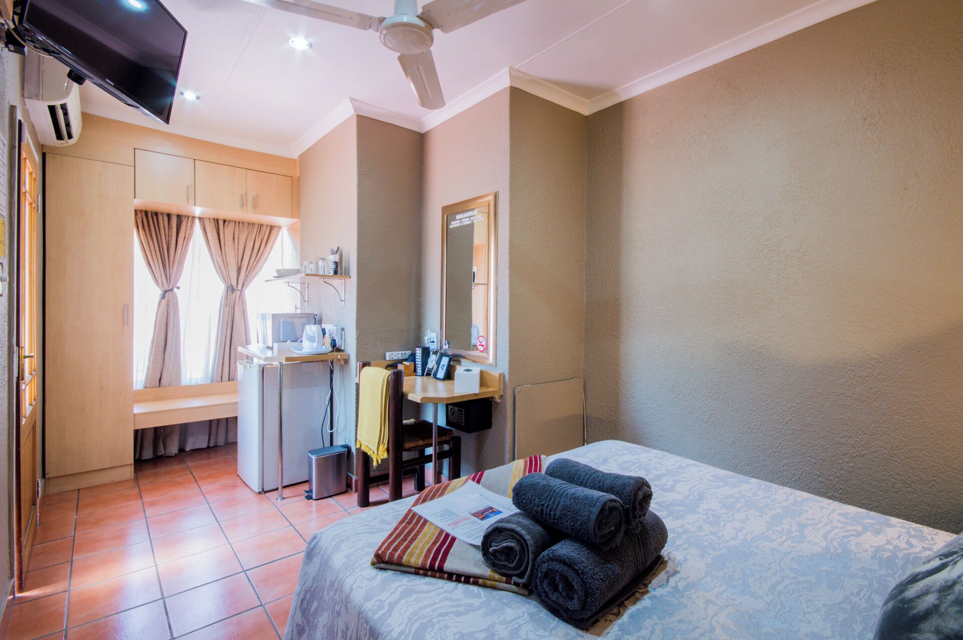 Habitación de hotel con cama, escritorio con computadora, espejo y ventana con cortinas.