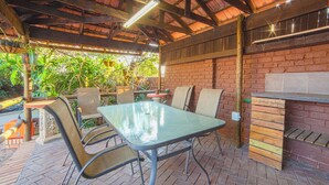 Eine Terrasse im Freien mit Pflasterboden, Metallstühlen, einem Glastisch und einem Grill aus Holz.