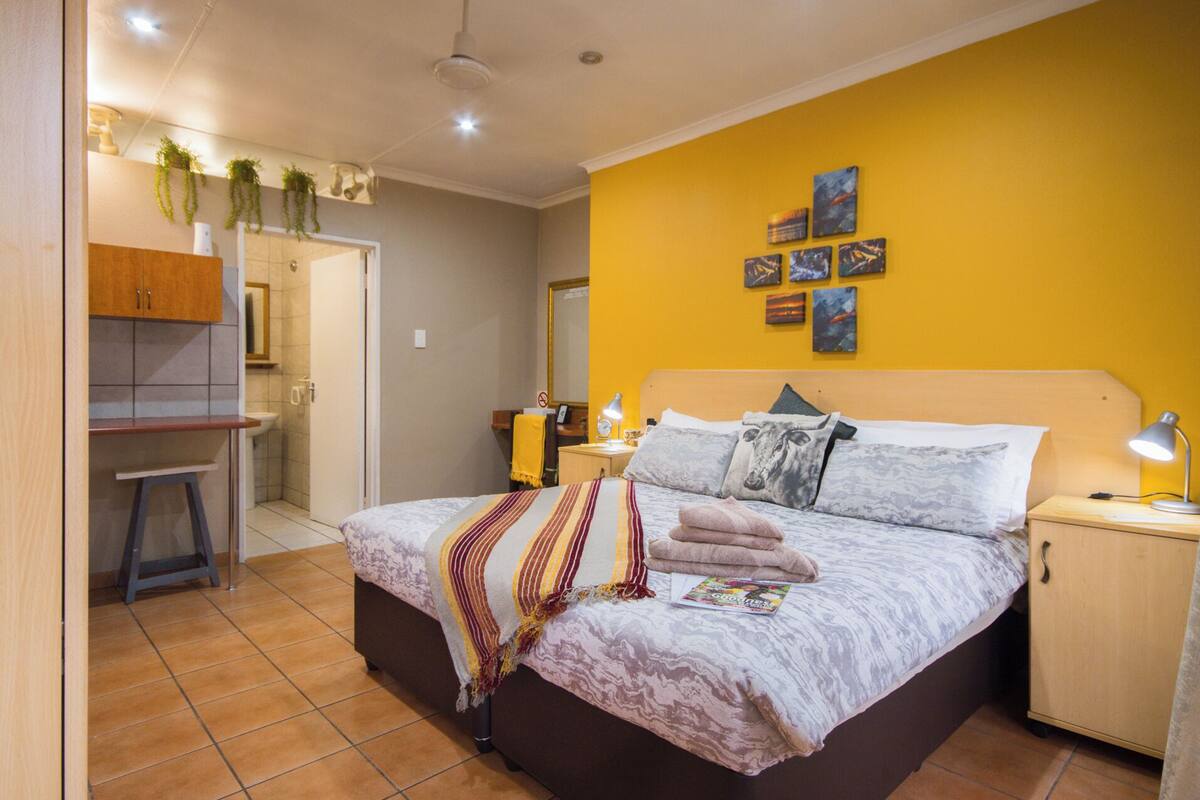 Een slaapkamer met een bed, nachtkastjes, een bureau, een stoel en een zichtbare badkamer door een geopende deur.