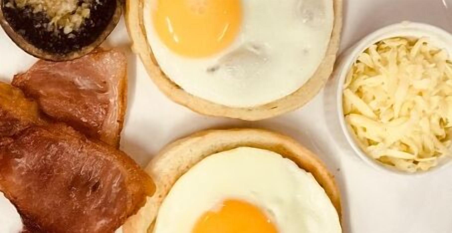 A breakfast plate with two eggs, bacon, and shredded cheese.