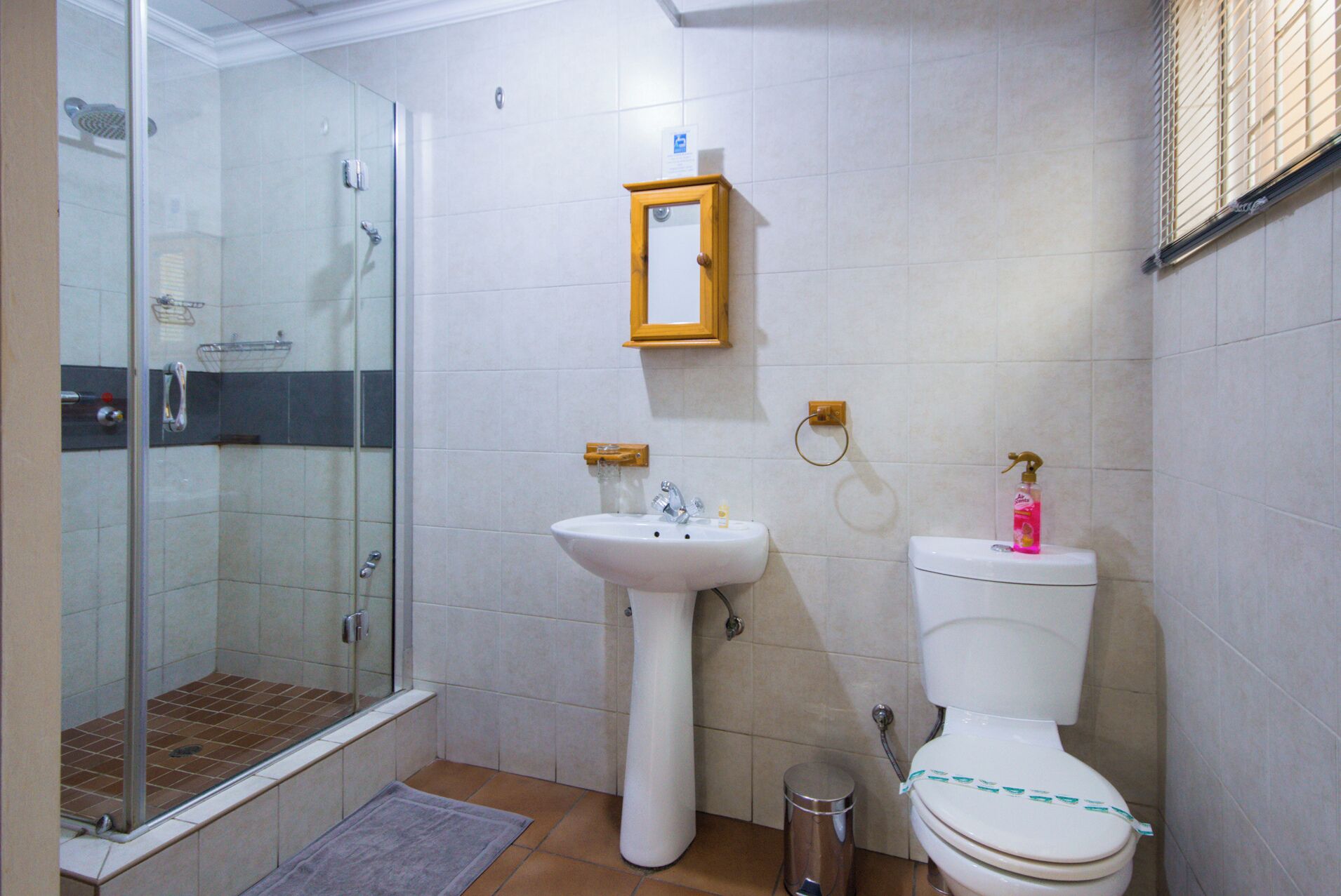Un baño con cabina de ducha de vidrio, lavamanos pedestal y retrete.