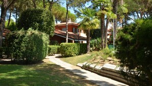 A house surrounded by lush greenery, including trees and bushes. - Nice apartment for 6 people with pool, A/C, TV, balcony and pets allowed (Bibione)
