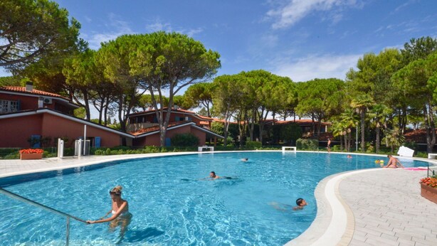 A swimming pool with people swimming and relaxing, surrounded by trees and buildings. - Nice apartment for 6 people with pool, A/C, TV, balcony and pets allowed (Bibione)