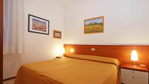 Une chambre d’hôtel comprenant un lit, deux tables de chevet, une petite table, une lampe et deux tableaux encadrés accrochés au mur.