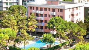 A hotel with a pool surrounded by trees, a view of the sea, and balconies with laundry hanging. - Cosy apartment for 5 people with A/C, pool, TV, balcony and pets allowed (San Michele Al Tagliamento)
