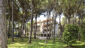 A multi-story building with balconies, surrounded by a grassy area with trees. - Cosy apartment for 5 guests with A/C, TV, balcony and pets allowed (San Michele Al Tagliamento)