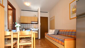 A compact living space with a kitchenette, a dining area with wooden furniture, and a sofa with a plaid blanket. - Cosy apartment for 5 guests with A/C, TV, balcony and pets allowed (San Michele Al Tagliamento)