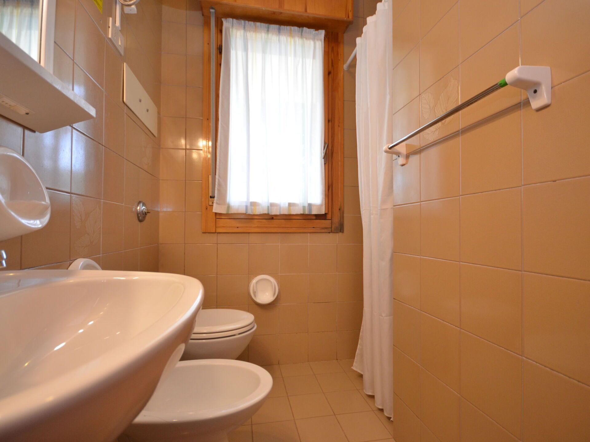 Une salle de bain avec un lavabo, deux toilettes, une fenêtre avec un rideau et un porte-serviettes.