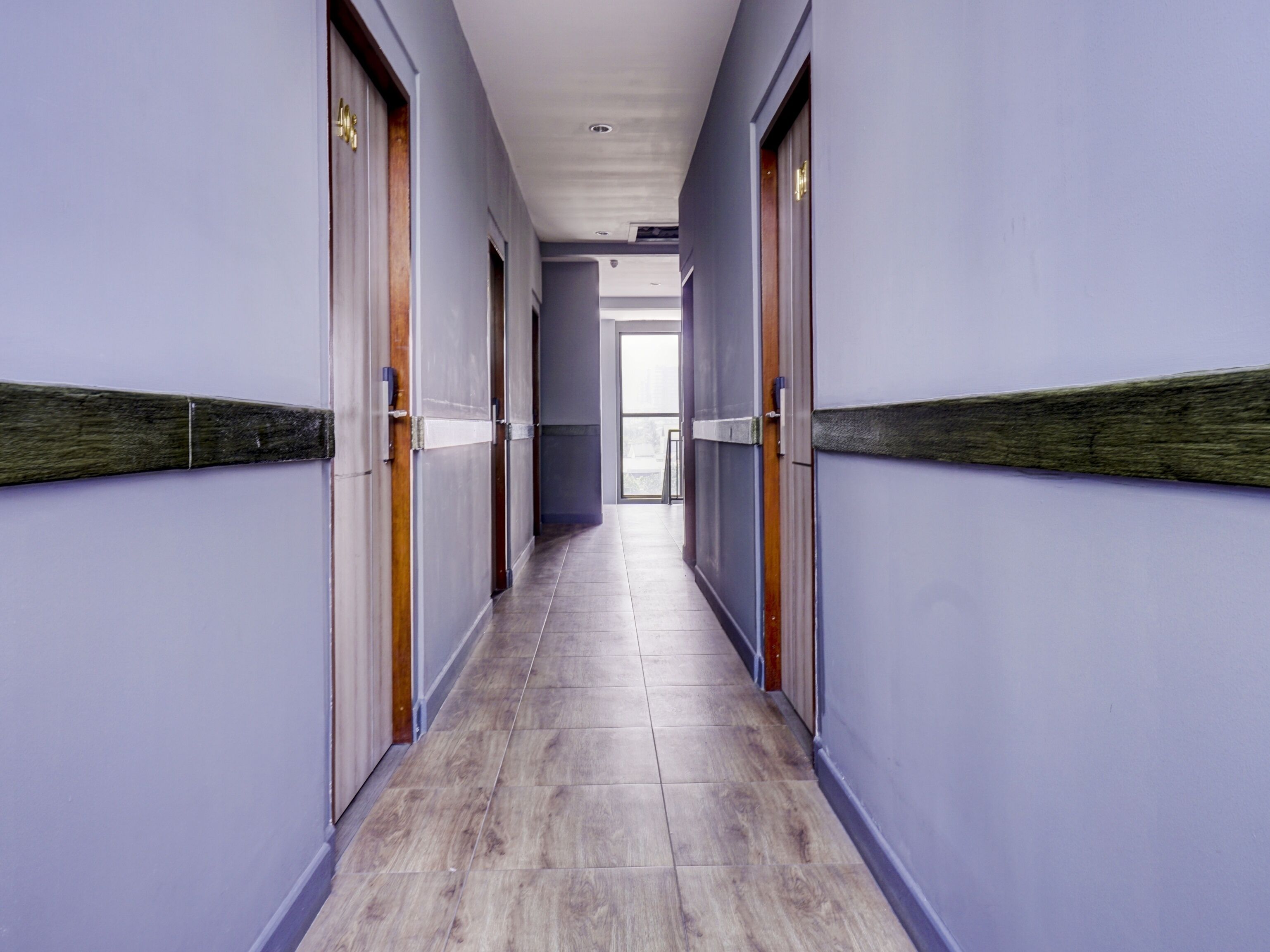 A long, narrow hallway with wooden doors and light-colored wooden flooring.