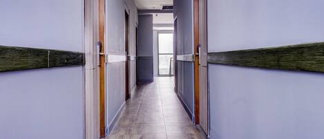 A long, narrow hallway with wooden doors and light-colored wooden flooring.