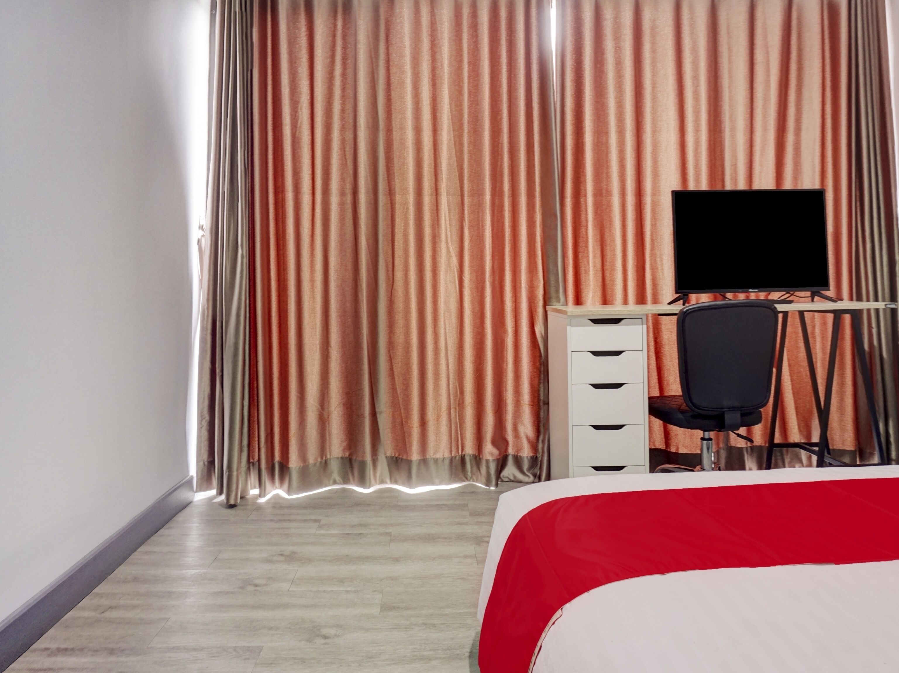 Una habitación de hotel con una cama, un escritorio con silla, un televisor y cortinas.
