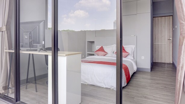 Ein modernes Hotelzimmer mit Schreibtisch, einem Bett mit roten Kissen und Blick auf den Himmel durch eine Glastür.