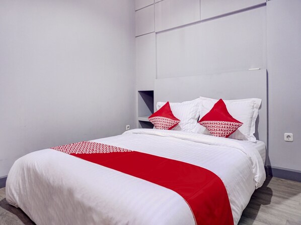 A neatly made bed with white and red bedding, a headboard with built-in shelves, and a plain white wall.