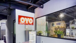 Ein Empfangsbereich mit modernem Design, mit einem großen 'OYO'-Schild, einer Uhr und einem Empfangstresen mit Mikrofon.