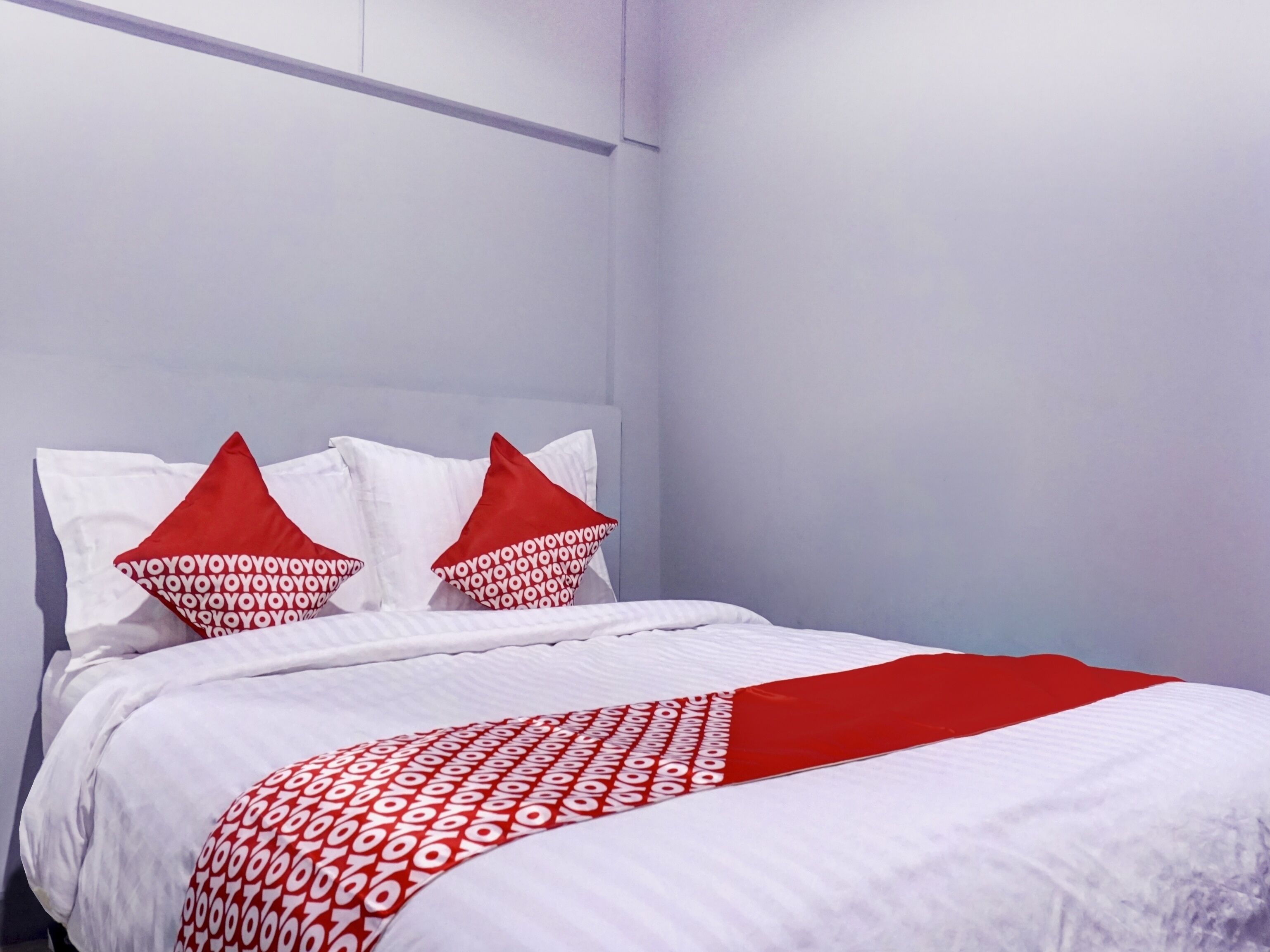 Cama bem arrumada com roupa de cama branca e detalhes vermelhos, incluindo almofadas e manta.